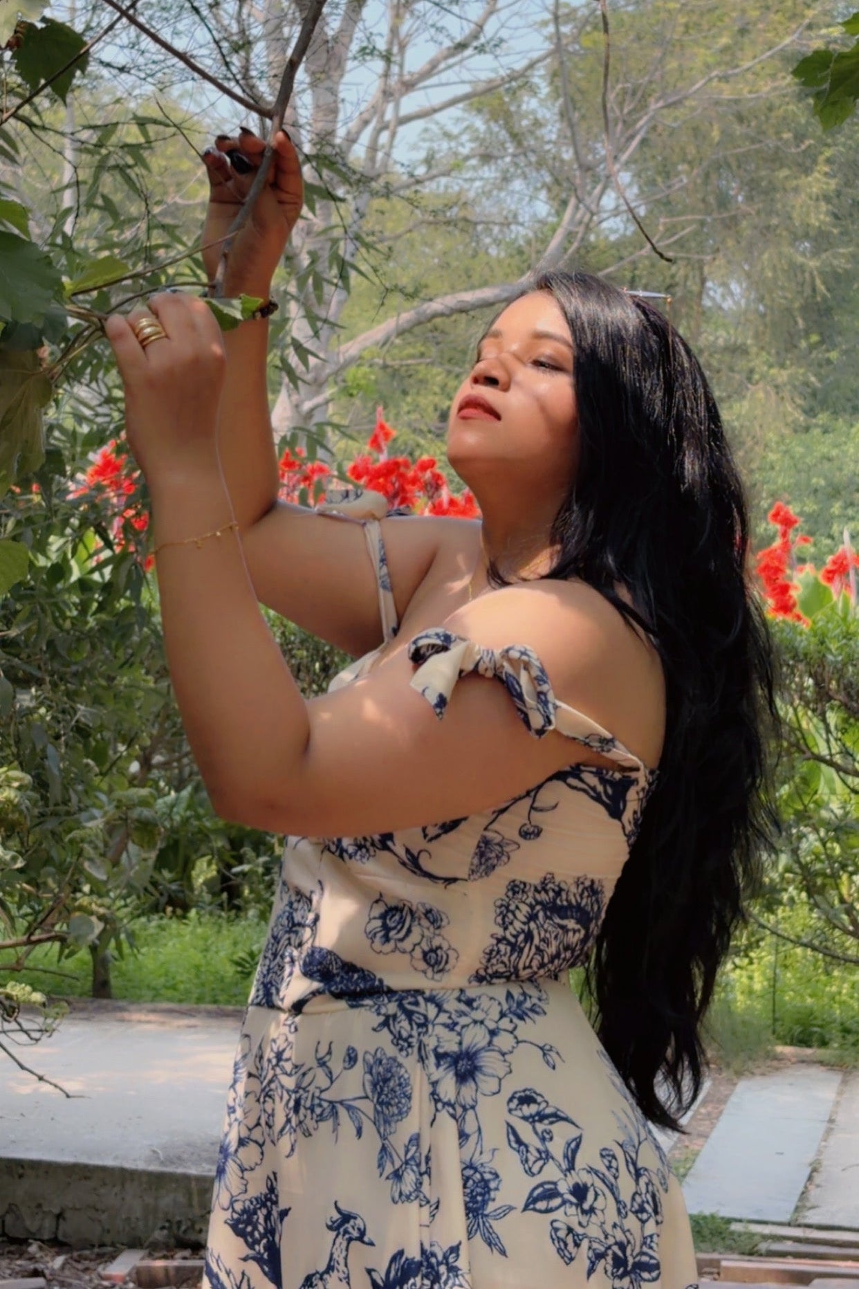 Woman in a floral dress standing outdoors with greenery and flowers in the background
