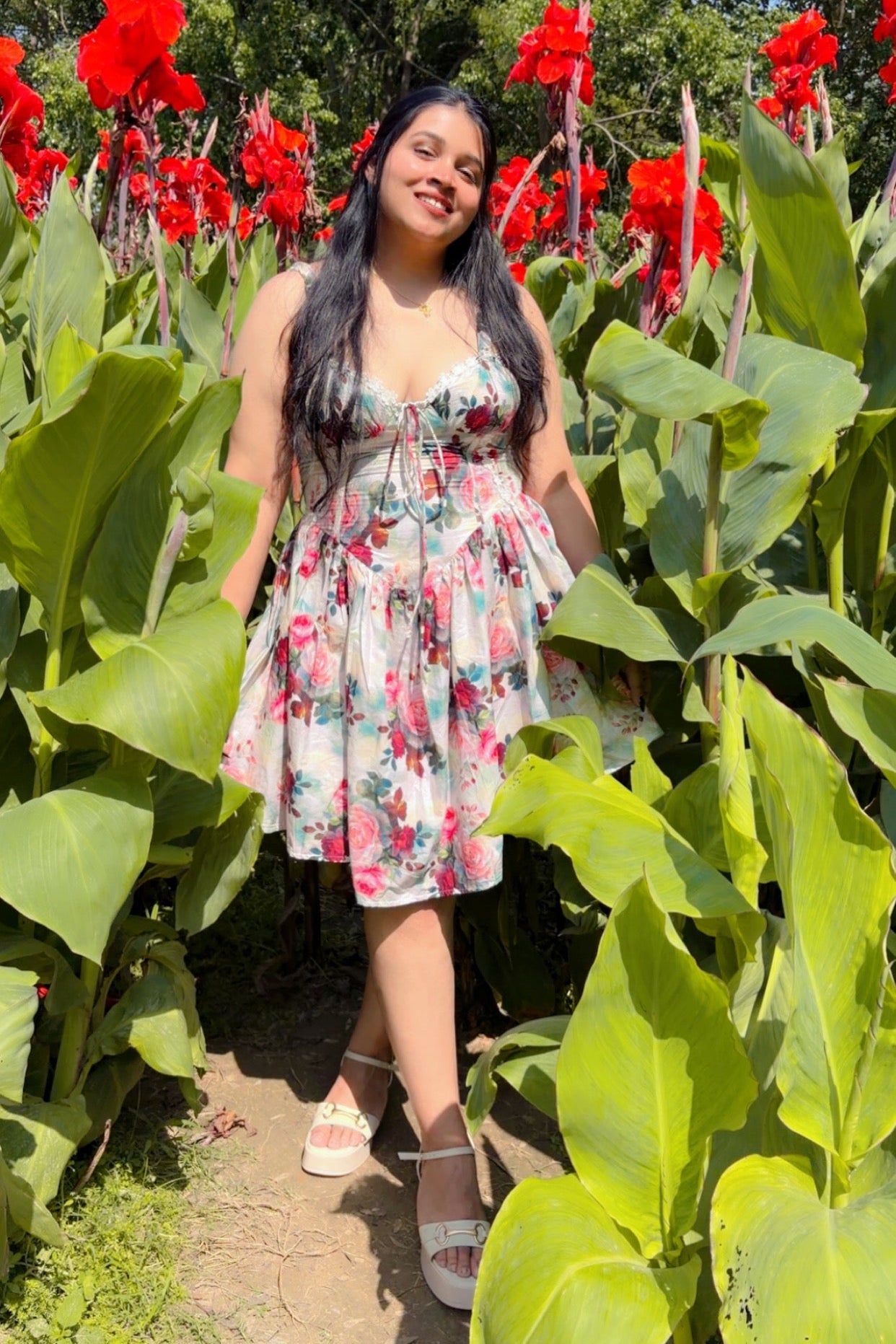 Woman in a floral dress standing among red flowers and green foliage