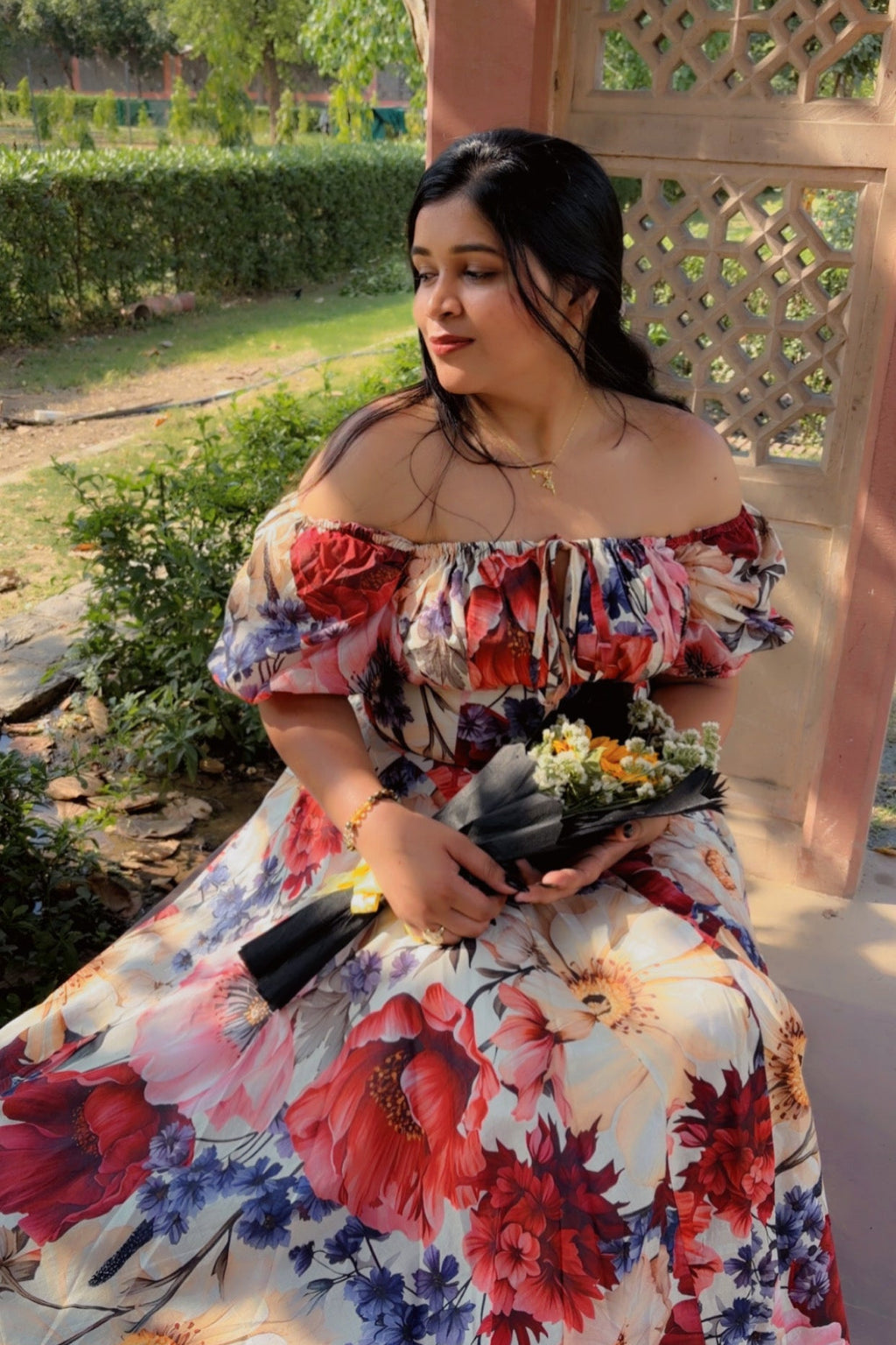 Woman in a floral dress sitting outdoors with greenery in the background