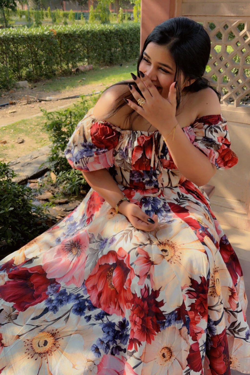 Woman in a floral dress sitting outdoors with greenery in the background
