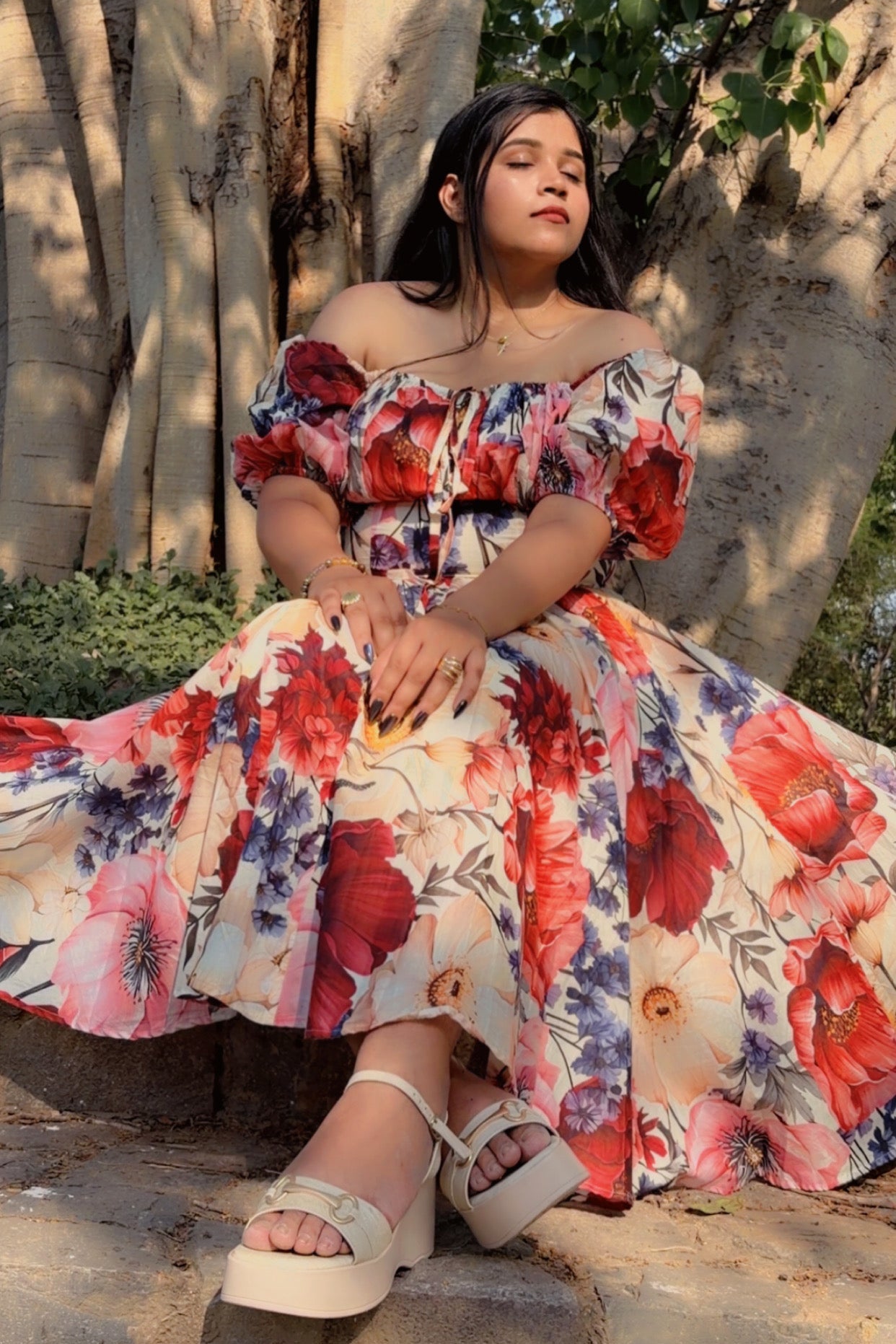 Woman in a floral dress sitting under a tree