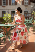 Woman in a floral dress sitting at an outdoor table with a red and white striped awning above.