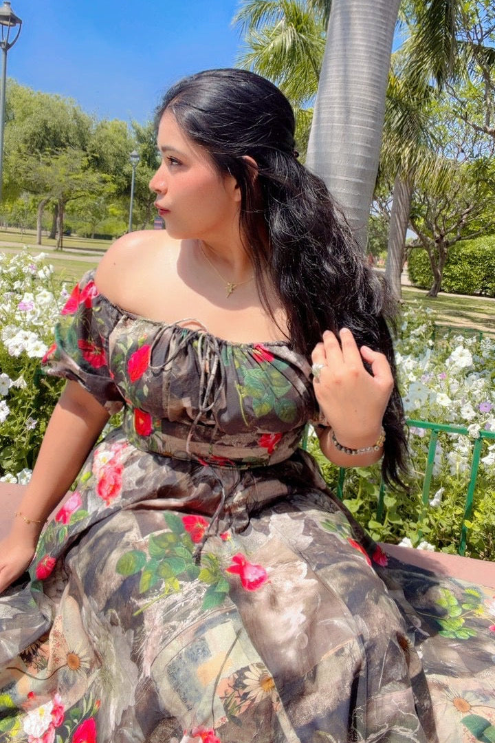 Woman in a floral dress sitting outdoors with greenery and flowers in the background