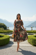 Woman in a floral dress standing in a garden with mountains in the background